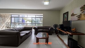 A living room with leather sofas, a glass coffee table, a TV, and a painting on the wall. - Apartamento em Fortaleza a 300m da Praia do Futuro (Fortaleza)