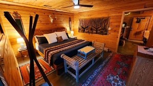 Une chambre confortable dans un chalet en rondins, avec un lit, un banc, un tapis et un ventilateur de plafond.