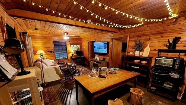 L’intérieur d’un chalet accueillant, avec un plancher en bois, une table à manger en bois, un canapé, un téléviseur et une bibliothèque.