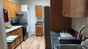 Una cocina con armarios de madera, un refrigerador de acero inoxidable, una estufa a gas y un lavamanos con escurreplatos.