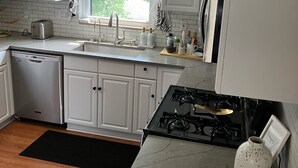 A modern kitchen with white cabinets, a stainless steel dishwasher, a gas stove, and a window with curtains. - Stunning 2-bedroom Home w/ WiFi, AC in Brookline Pittsburgh,PA (Pittsburgh)