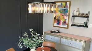 A dining area with a round table, chairs, a vase with plants, a colorful abstract painting, a cabinet with shelves, and a hanging light fixture. - Stunning 2-bedroom Home w/ WiFi, AC in Brookline Pittsburgh,PA (Pittsburgh)