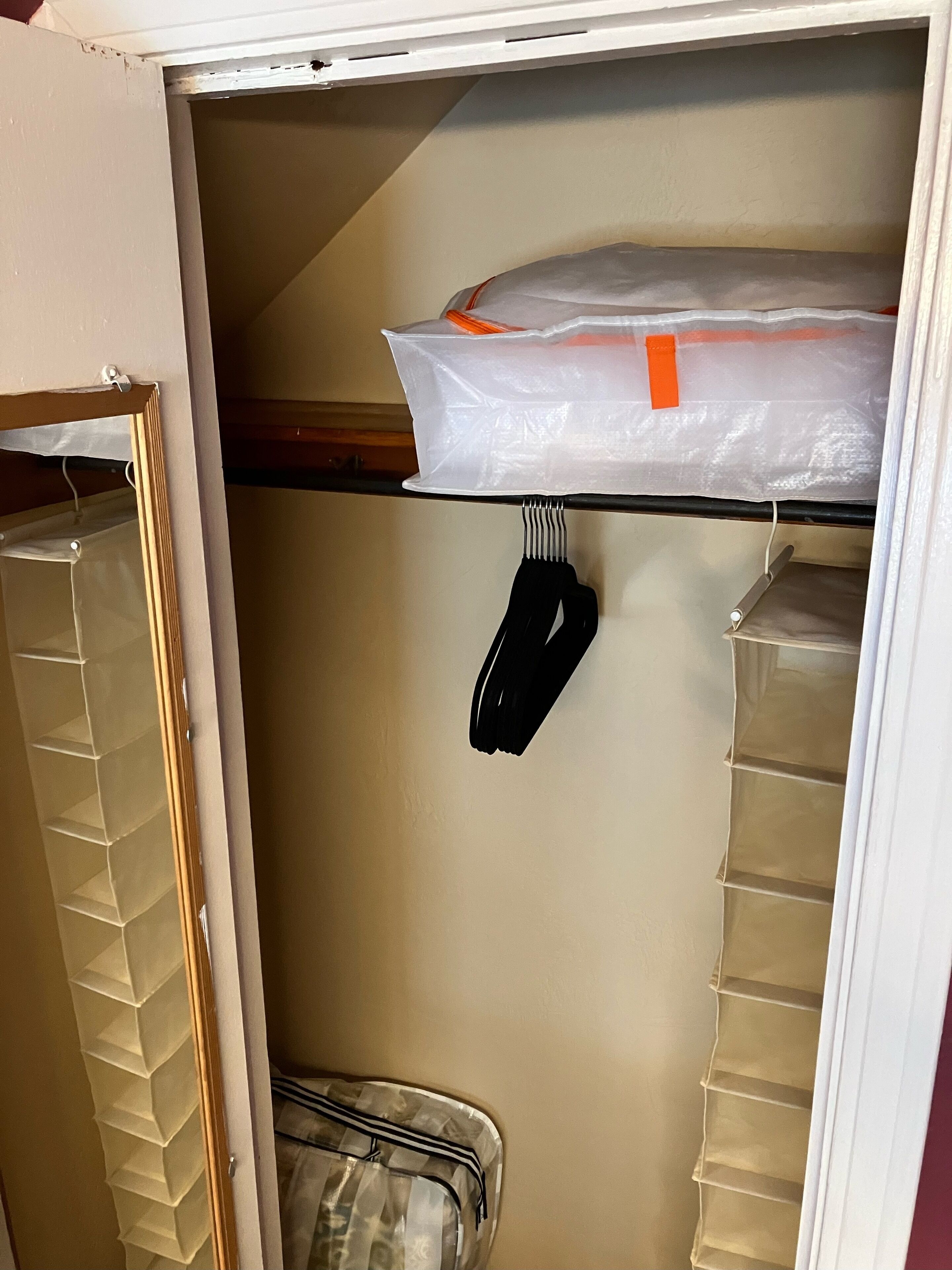 Un armario para guardado con estantes, una percha y una bolsa de plástico en el estante superior.