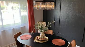 A dining area with a black table, two brown chairs, a vase with a plant, and a chandelier.