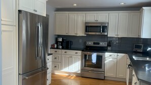 A modern kitchen with stainless steel appliances, white cabinetry, and a wooden floor. - Enjoyable a cabin on the Black river with WiFi in Ludlow for a cozy stay (Ludlow)