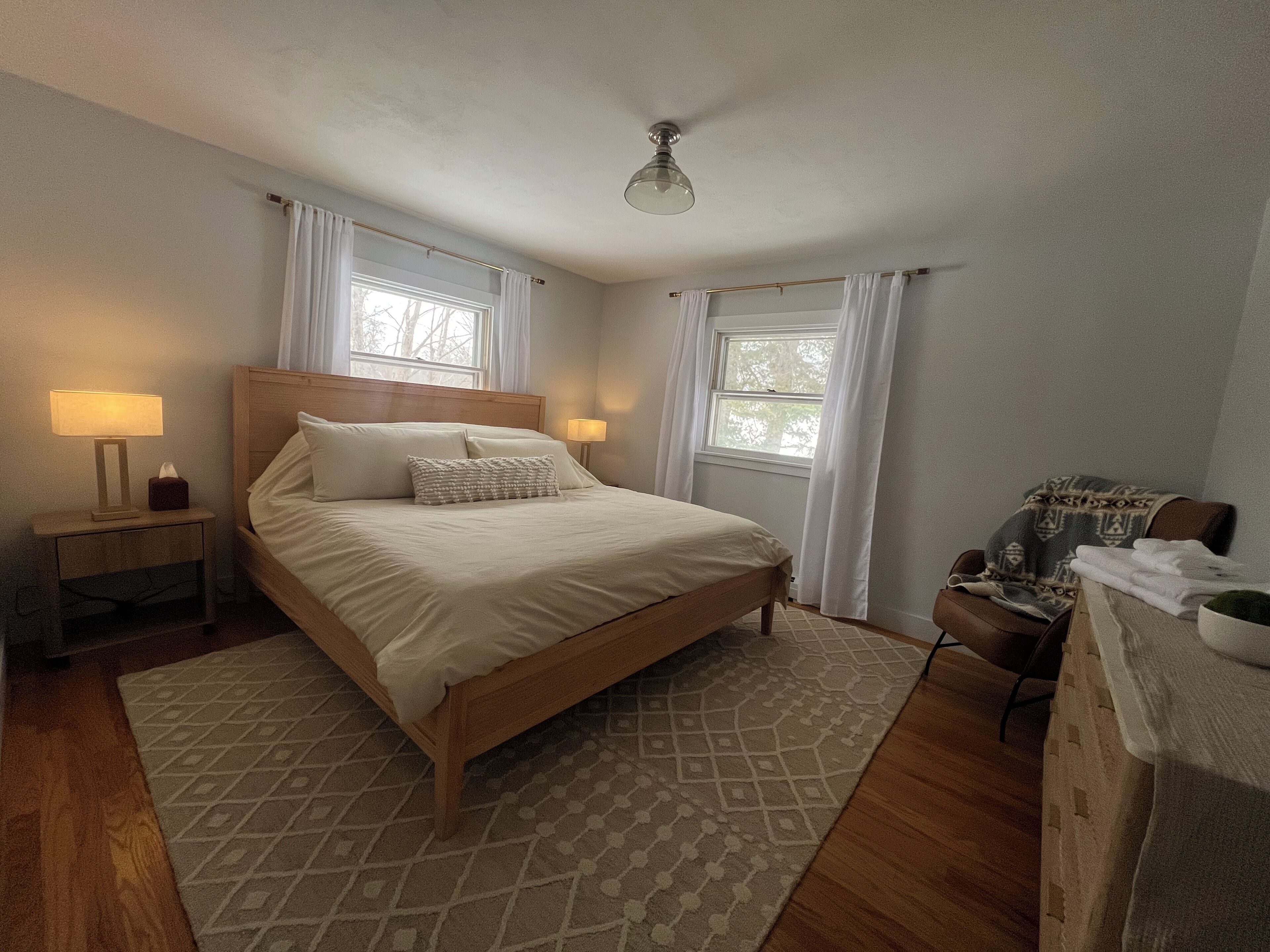 Una camera da letto con un letto di legno, due lampade sui comodini, un comodino, un tappeto decorato e una finestra con tende.