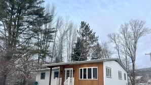 A small, single-story cabin with a porch and a covered entryway, surrounded by snow-covered ground and trees. - Enjoyable a cabin on the Black river with WiFi in Ludlow for a cozy stay (Ludlow)