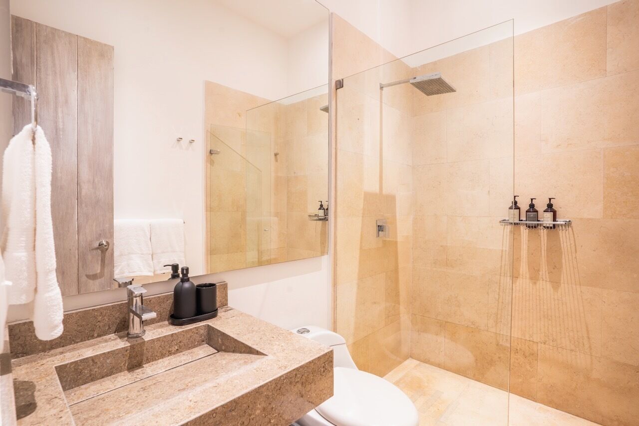A modern bathroom with a glass-enclosed shower, a marble sink, and a toilet.