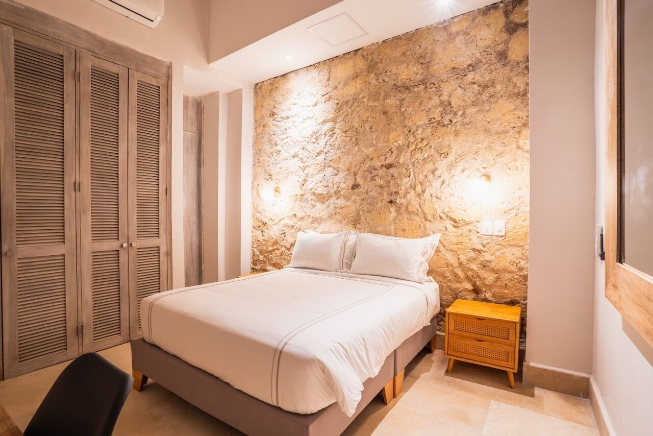Une chambre avec un mur en pierre, un lit, une table de chevet en bois et une armoire.