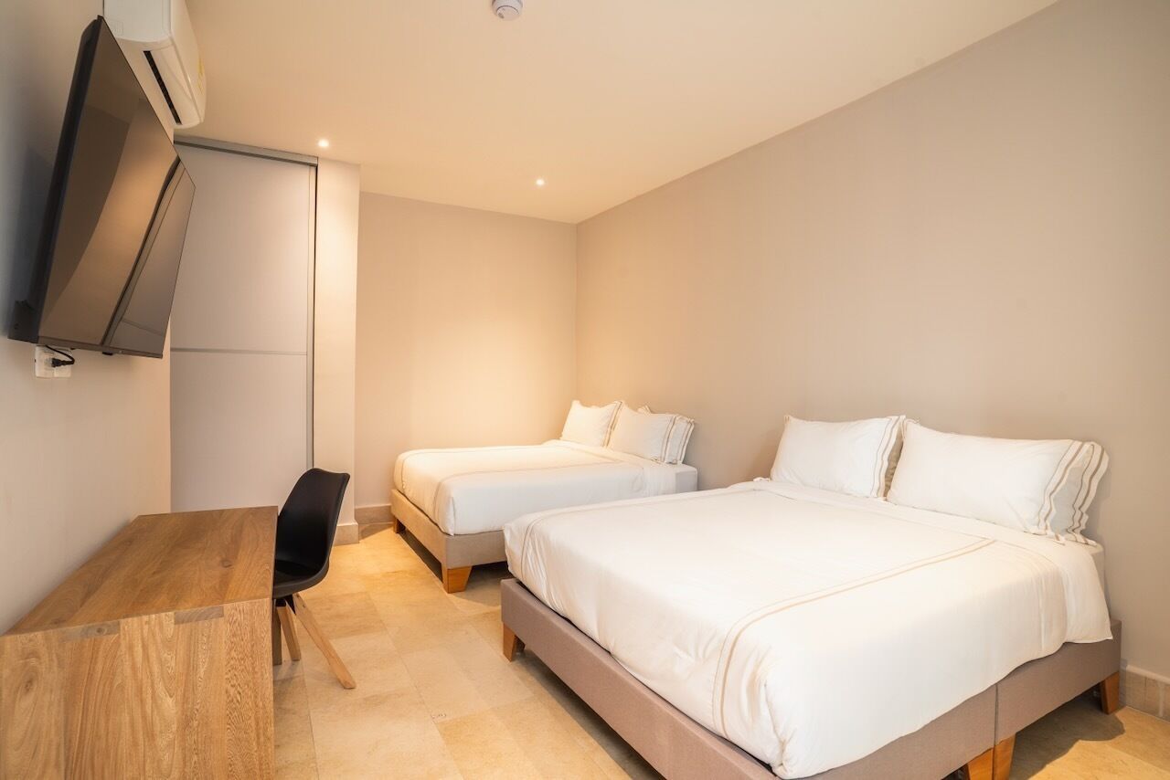 A hotel room with two single beds, a wooden desk, a chair, and a flat-screen TV mounted on the wall.