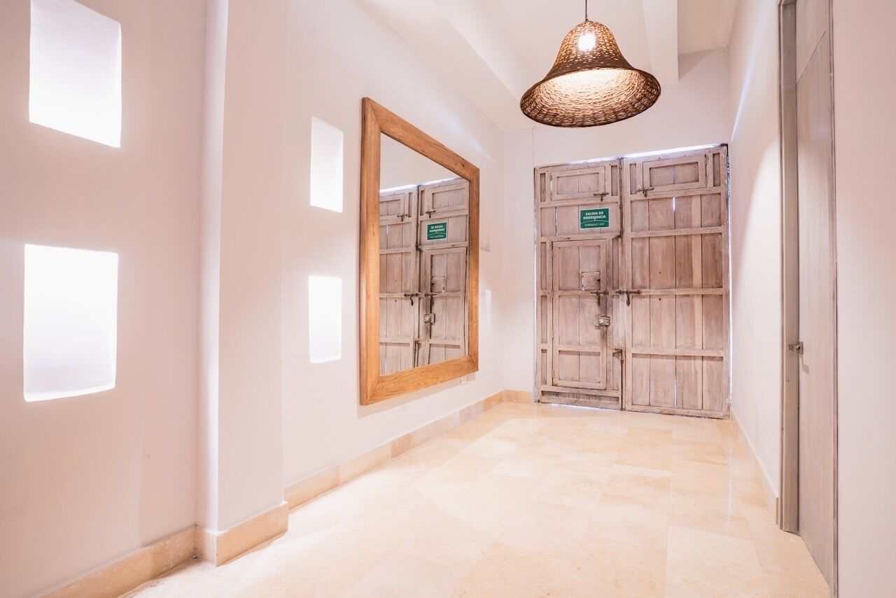 A hallway with a large mirror, wooden doors, and a hanging light fixture.