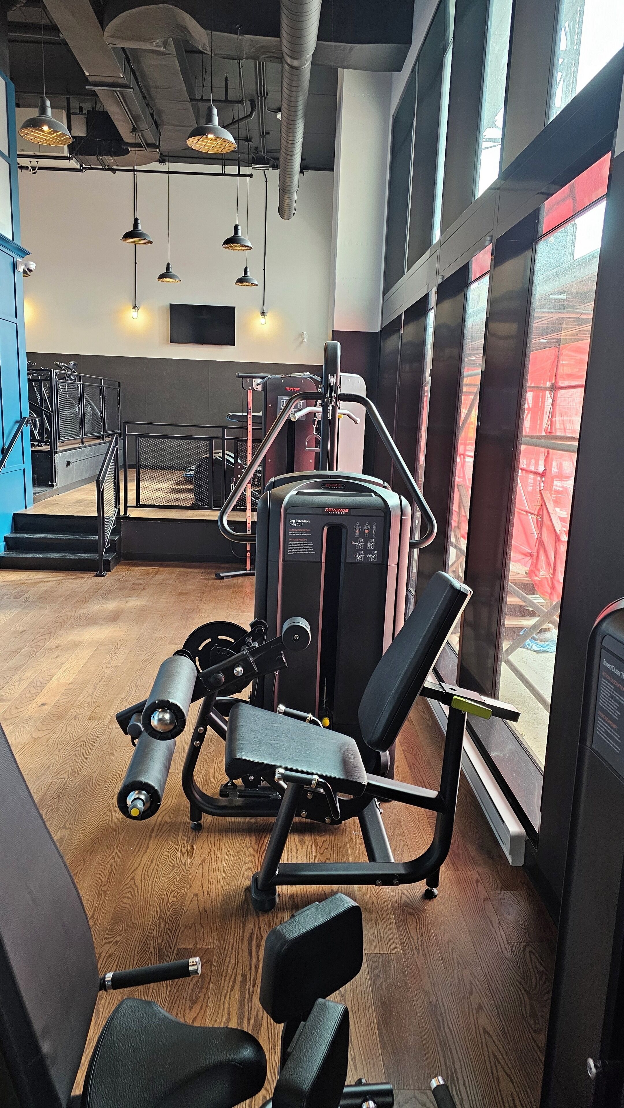 Un gimnasio con equipo de ejercicio, una escalera y ventanas amplias.
