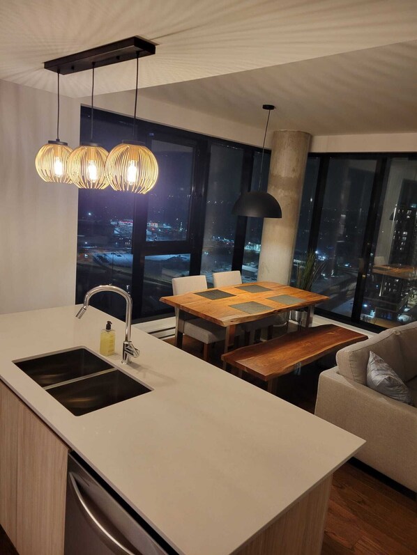 A modern kitchen with a large island, a dining area with a wooden table, and a view of the city at night.
