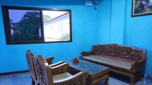 A room with a blue wall, a wooden sofa, a matching wooden table, and a window with a view of a building and trees. - Ban Kai Na (Hua Hin)