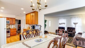 Un salón espacioso con una mesa de comedor, sillas de madera, una araña y un sofá.