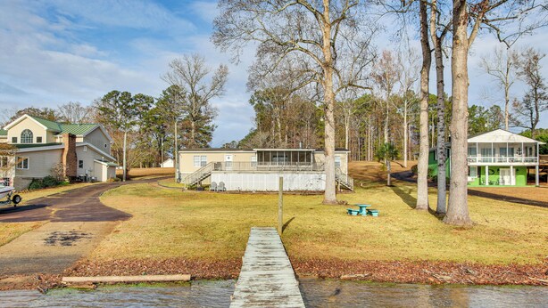 A waterfront property with a wooden dock leading to a house with a green roof and a large window. - Saluda River Retreat w/ Boat Ramp & Water Views! (Prosperity)