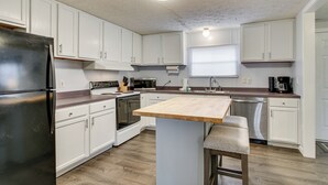A modern kitchen with white cabinets, stainless steel appliances, a wooden island, and a bar stool. - Saluda River Retreat w/ Boat Ramp & Water Views! (Prosperity)