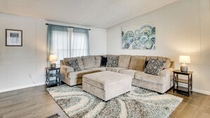 A living room with a sectional sofa, a matching ottoman, two side tables with lamps, a large abstract painting, and a window with curtains. - Saluda River Retreat w/ Boat Ramp & Water Views! (Prosperity)