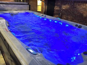 Ein Whirlpool mit blauer LED-Beleuchtung, einem Warnhinweis und einer Ziegelwand im Hintergrund.