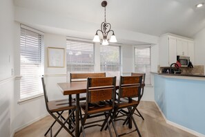 Un comedor con una mesa y sillas de madera, un candelabro y una cocina con armarios y un microondas.