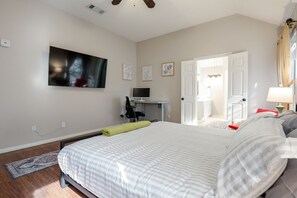 Un dormitorio con cama, escritorio, televisor y puerta que da a un baño.