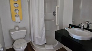 A bathroom with a toilet, a shower with a white curtain, a sink with a mirror, and a towel rack with rolled towels. - Varsity West (Centralia)