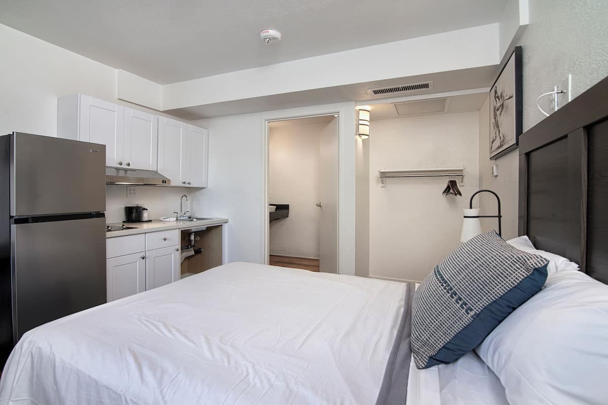 A compact hotel room with a bed, a kitchenette, and a bathroom.