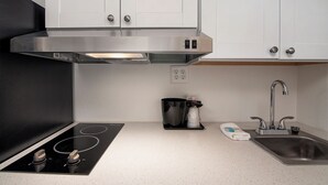 A modern kitchen with a black induction cooktop, stainless steel range hood, white cabinets, a sink, and a coffee maker. - Varsity West (Centralia)