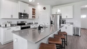 A modern kitchen with white cabinetry, stainless steel appliances, a central island with bar stools, and a pendant light. - Getaway home, Savannah spot (Port Wentworth)