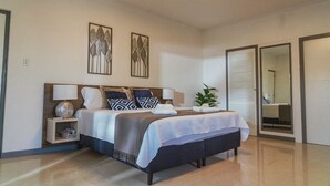 Ein modernes Schlafzimmer mit einem großen Bett, zwei Nachttischen, einem Beistelltisch und einer Topfpflanze.