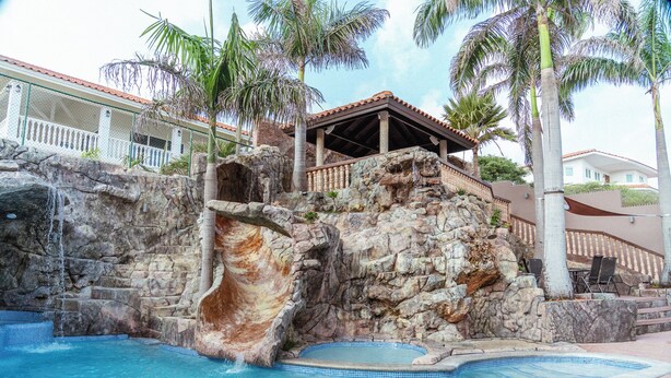 Ein Pool mit Wasserfall, umgeben von Steinmauern und Palmen.