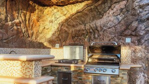 Eine Außenküche mit Steinrückwand, integriertem Grill und Pizzaofen.