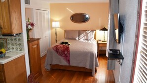 Quarto de hotel com cama, televisão, escrivaninha com luminária, espelho e janela com persianas.
