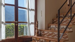 A staircase with patterned steps leading to a landing, a wooden door with a view of greenery, and a wall-mounted air conditioning unit. - Can Palou Fornalutx (Fornalutx)