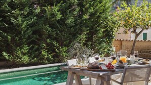 A dining table with food and drinks by a pool, surrounded by greenery. - Can Palou Fornalutx (Fornalutx)