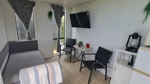 A compact room with a sofa, a small table, two chairs, a TV, and a cabinet. - Marvelous cabin with AC in Helena Bay (Helena Bay)