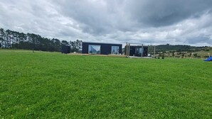 A modern building with large glass windows and a flat roof, situated in a grassy field with a playground in the background. - Marvelous cabin with AC in Helena Bay (Helena Bay)