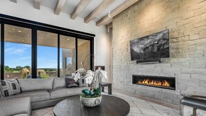 Una sala de estar moderna con una chimenea de piedra, un ventanal grande y una mesa de centro redonda con una planta.
