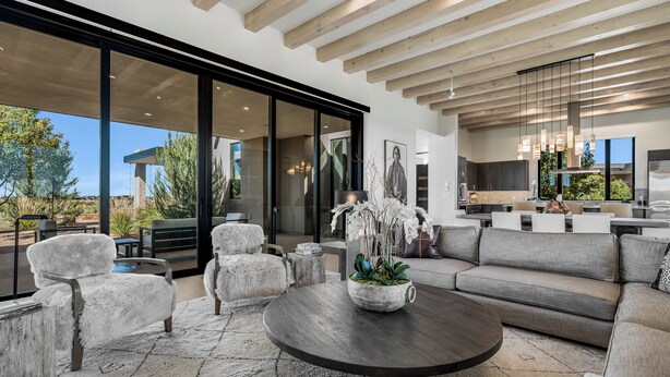 Una sala de estar moderna con un sofá grande, dos sillones y una mesa de centro. Hay un ventanal con vistas al exterior.