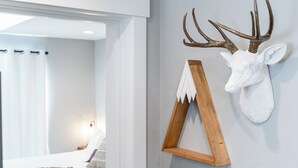 A room with a bed, a wooden headboard, and a wall-mounted deer head with antlers.