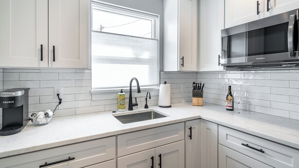 A modern kitchen with white cabinets, a stainless steel microwave, and a coffee maker.