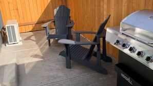 A backyard with a grill, two Adirondack chairs, and a portable heater.
