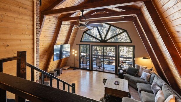 A cozy loft-style room with a wooden interior, a large window, and a flat-screen TV. - Sweetin Summit Retreat (Duck Creek Village)