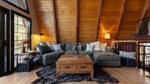 A cozy loft-style living room with a wooden ceiling, a sectional sofa, a coffee table, and a black fur rug. - Sweetin Summit Retreat (Duck Creek Village)
