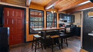 A rustic kitchen with a wooden ceiling, a red door, a large window, and a bar area with stools. - Sweetin Summit Retreat (Duck Creek Village)