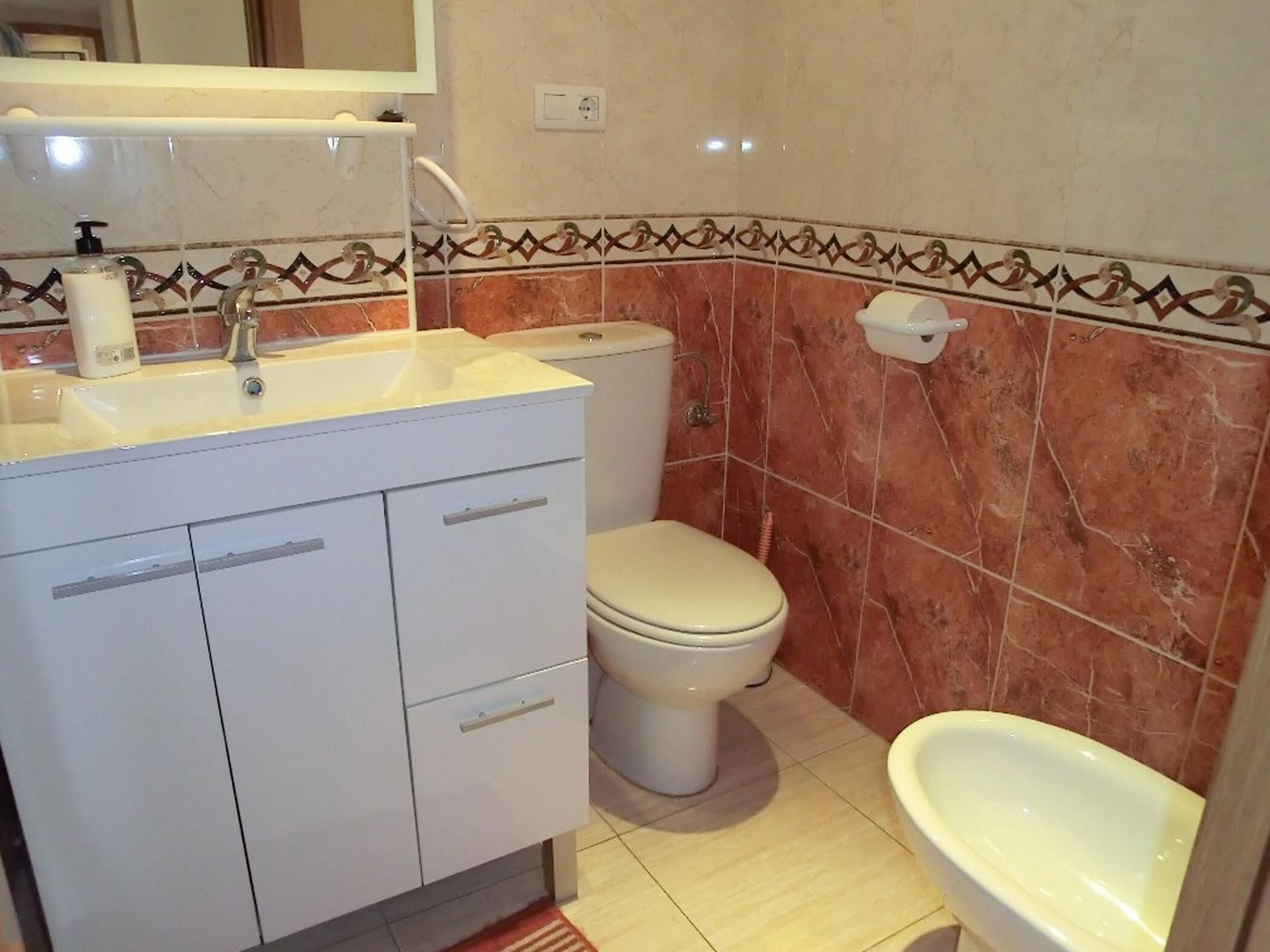 A bathroom with a white sink, toilet, and bidet. The walls have a patterned tile design.
