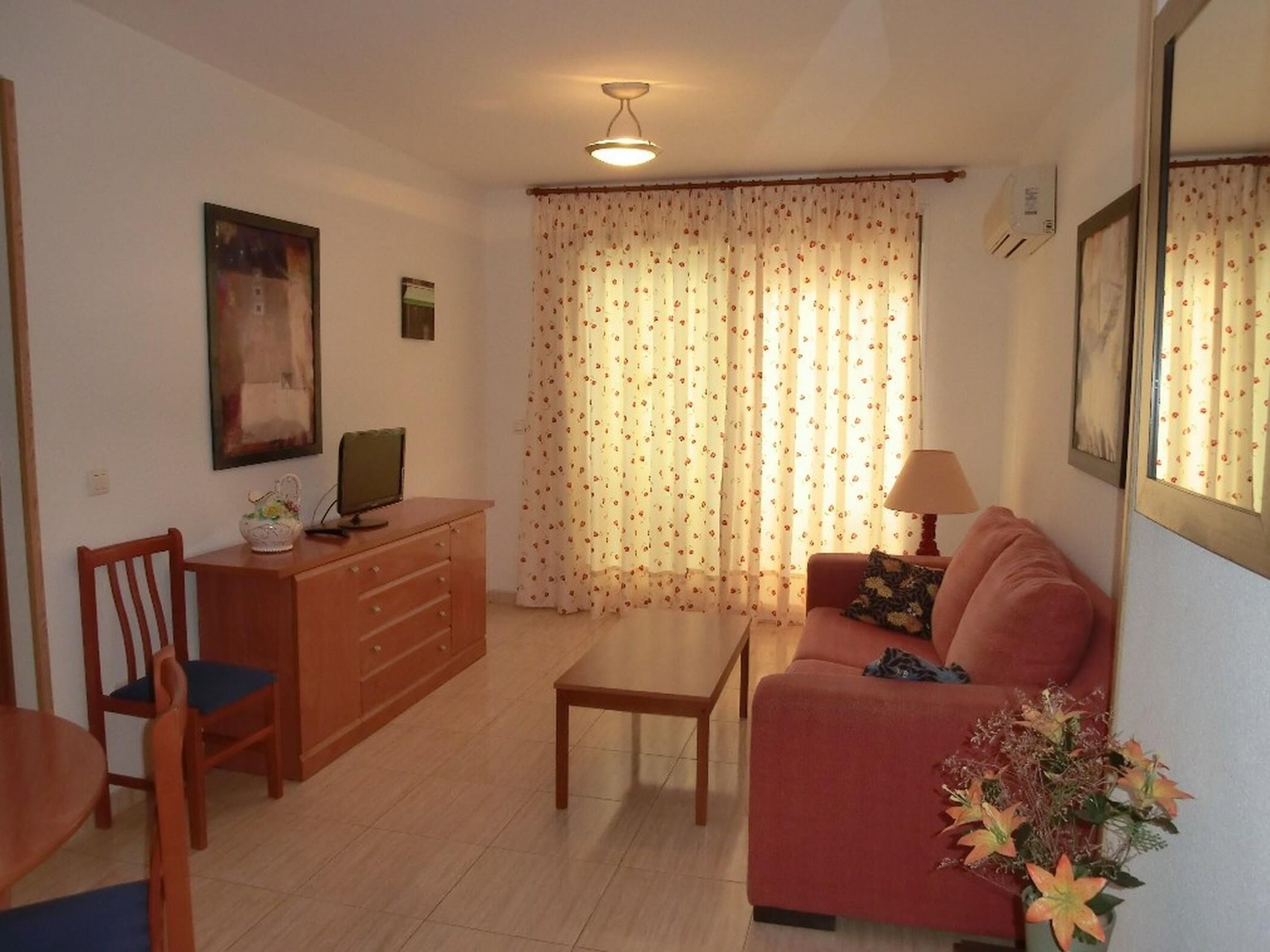Ein Wohnzimmer mit einer Couch, einem Couchtisch, einem Fernseher auf einer Holzkommode und einer Lampe.