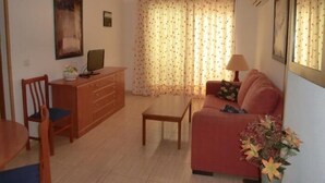 Una sala de estar con sofá, mesa de comedor, televisor en un mueble y ventana con cortinas.