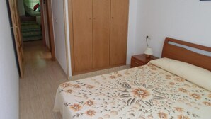 Un dormitorio con un armario de madera, una mesita de noche con lámpara y una colcha estampada.