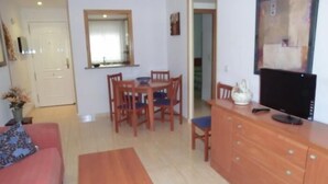 A compact living space with a dining area, a sofa, a TV, and a wooden cabinet.